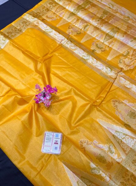 A mustard yellow Tussar silk Bhagalpuri saree with a broad gold zari border, featuring floral Meenakari work in pink and green, laid out on a dark surface.