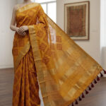 Mustard yellow Chanderi silk Bhagalpuri saree featuring maroon geometric embroidery, a gold zari border, and maroon pom-poms on the pallu
