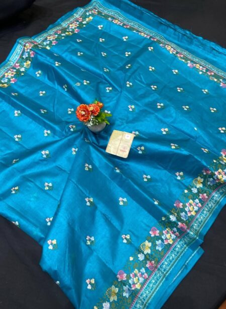 A vibrant feroza turquoise blue pure Bhagalpuri Munga silk handloom saree from Bhavya Lakshmi Fabrics featuring detailed multicolored floral embroidery scattered butis and an ornate floral border.