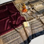 A close-up view of a rich wine-colored Tussar Ghicha pure silk handloom saree from Bhavya Lakshmi Fabrics featuring detailed black and beige Madhubani print panels and an elaborate storytelling pallu.