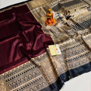 A close-up view of a rich wine-colored Tussar Ghicha pure silk handloom saree from Bhavya Lakshmi Fabrics featuring detailed black and beige Madhubani print panels and an elaborate storytelling pallu.