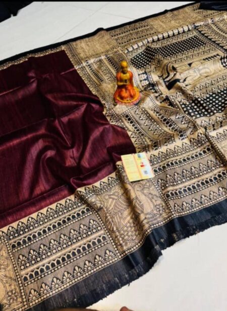A close-up view of a rich wine-colored Tussar Ghicha pure silk handloom saree from Bhavya Lakshmi Fabrics featuring detailed black and beige Madhubani print panels and an elaborate storytelling pallu.