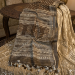 Elegant earth brown semi-linen Bhagalpuri saree featuring white block prints, architectural pallu details, and pompom tassels.