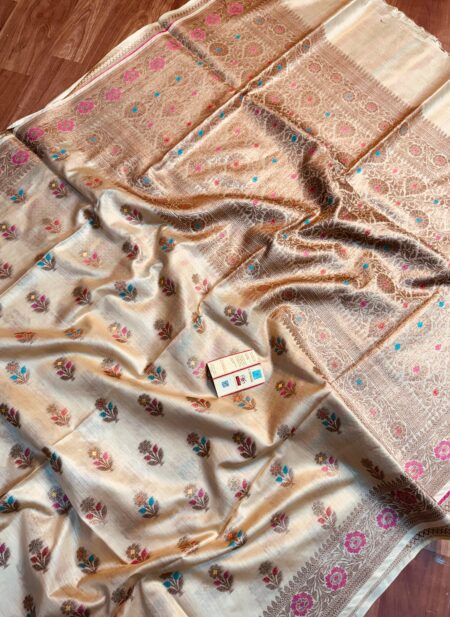 Natural beige gold pure Bhagalpuri Munga silk saree from Bhavya Lakshmi Fabrics featuring multi-color floral Meenakari butis and an intricate gold zari border, spread on a wooden floor