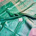 Sea green pure Bhagalpuri Munga silk saree from Bhavya Lakshmi Fabrics featuring small multi-color floral butis and an intricate gold zari border, spread on a wooden floor.