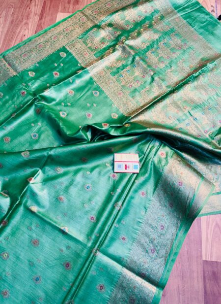 Sea green pure Bhagalpuri Munga silk saree from Bhavya Lakshmi Fabrics featuring small multi-color floral butis and an intricate gold zari border, spread on a wooden floor.
