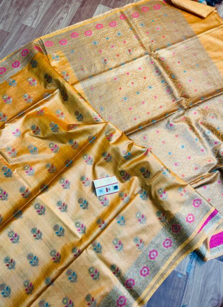 Golden yellow pure Bhagalpuri Munga silk saree featuring small multi-color floral butis, an intricate gold zari border with pink accents, and a heavily woven zari pallu, spread on a floor.
