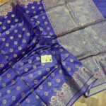 Vibrant royal blue pure Bhagalpuri Munga silk saree from Bhavya Lakshmi Fabrics featuring multi-color floral butis and an intricate gold zari border, spread on a wooden floor.