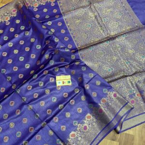 Vibrant royal blue pure Bhagalpuri Munga silk saree from Bhavya Lakshmi Fabrics featuring multi-color floral butis and an intricate gold zari border, spread on a wooden floor.