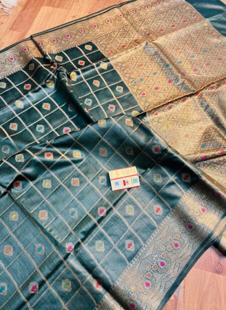 Vibrant bottle green pure Bhagalpuri Munga silk saree from Bhavya Lakshmi Fabrics featuring gold zari checks with multi-color floral Meenakari butis and an intricate gold zari border, spread on a wooden floor.