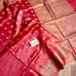 Vibrant crimson red pure Bhagalpuri Munga silk saree from Bhavya Lakshmi Fabrics featuring multi-color floral Meenakari butis and an intricate gold zari border, spread on a wooden floor.
