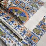 Off-white dupion slub silk unstitched suit material featuring traditional green, orange, and blue Madhubani fish prints.