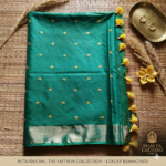 A luxurious emerald green Kota silk saree from Bhavya Lakshmi Fabrics featuring detailed golden embroidered butis, a wide gold zari border, and bright yellow edge tassels.