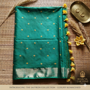 A luxurious emerald green Kota silk saree from Bhavya Lakshmi Fabrics featuring detailed golden embroidered butis, a wide gold zari border, and bright yellow edge tassels.