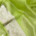 A close-up view of a vibrant Lime Green Organza Banarasi Saree from Bhavya Lakshmi Fabrics featuring detailed handwoven silver zari floral borders and delicate scattered butis.