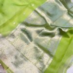 A close-up view of a vibrant Lime Green Organza Banarasi Saree from Bhavya Lakshmi Fabrics featuring detailed handwoven silver zari floral borders and delicate scattered butis.