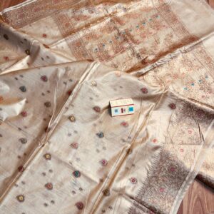 Natural beige Pure Bhagalpuri Muga silk saree featuring small multi-color floral butis, an intricate zari border, and a heavily woven floral pallu spread on a wooden floor.
