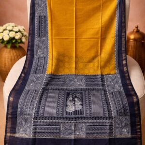 A mustard yellow Kota silk Bhagalpuri saree from Bhavya Lakshmi Fabrics featuring detailed black and white monochrome Madhubani art prints of a divine couple and peacocks.