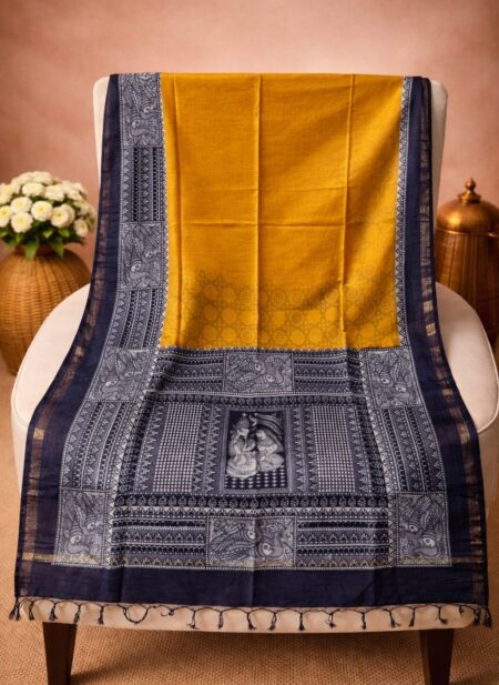A mustard yellow Kota silk Bhagalpuri saree from Bhavya Lakshmi Fabrics featuring detailed black and white monochrome Madhubani art prints of a divine couple and peacocks.