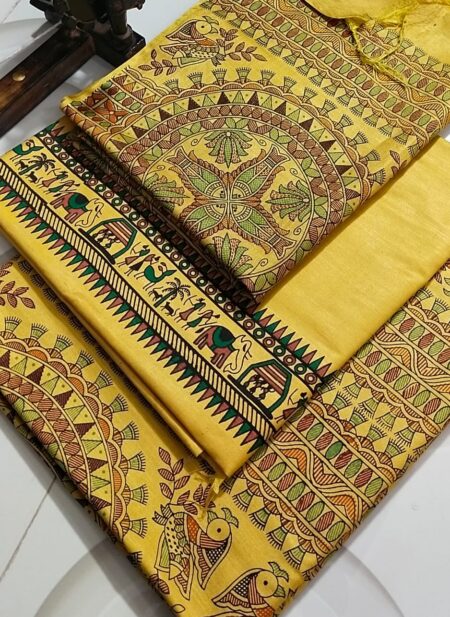 An unstitched mustard yellow Katan silk suit material set by Bhavya Lakshmi Fabrics featuring extensive multi-colored Madhubani prints of ceremonial elephants, ritual huts, and stylized birds with geometric circular borders.