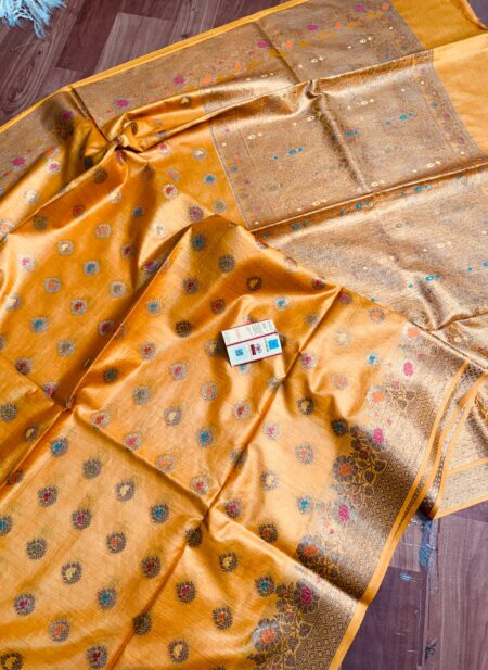 Vibrant mustard yellow pure Bhagalpuri Munga silk saree from Bhavya Lakshmi Fabrics featuring small multi-color Meenakari floral butis and an intricate gold zari border, spread on a wooden floor.