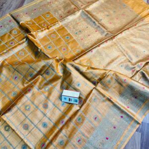 Vibrant mustard yellow pure Bhagalpuri Munga silk saree from Bhavya Lakshmi Fabrics featuring gold zari checks with multi-color floral Meenakari butis and an intricate gold zari border, spread on a wooden floor.