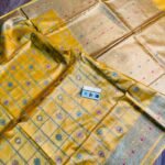 Vibrant mustard yellow pure Bhagalpuri Munga silk saree from Bhavya Lakshmi Fabrics featuring gold zari checks with multi-color floral Meenakari butis and an intricate gold zari border, spread on a wooden floor.