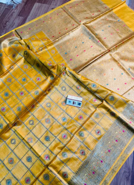 Vibrant mustard yellow pure Bhagalpuri Munga silk saree from Bhavya Lakshmi Fabrics featuring gold zari checks with multi-color floral Meenakari butis and an intricate gold zari border, spread on a wooden floor.