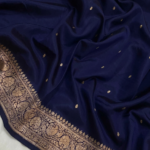 A semi-sheer Navy Blue Organza Banarasi Saree from Bhavya Lakshmi Fabrics, featuring handwoven golden zari butis and a grand floral border.