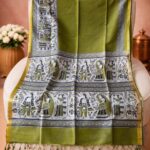 An olive green Kota silk Bhagalpuri saree from Bhavya Lakshmi Fabrics featuring detailed monochrome and olive Madhubani art prints of folklore figures and decorative borders.