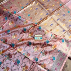 Elegant pastel peach pure Bhagalpuri Muga silk saree from Bhavya Lakshmi Fabrics featuring a multi-color floral Meenakari jaal and an intricate gold zari border, spread on a wooden floor.