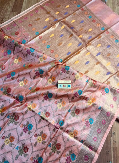 Elegant pastel peach pure Bhagalpuri Muga silk saree from Bhavya Lakshmi Fabrics featuring a multi-color floral Meenakari jaal and an intricate gold zari border, spread on a wooden floor.