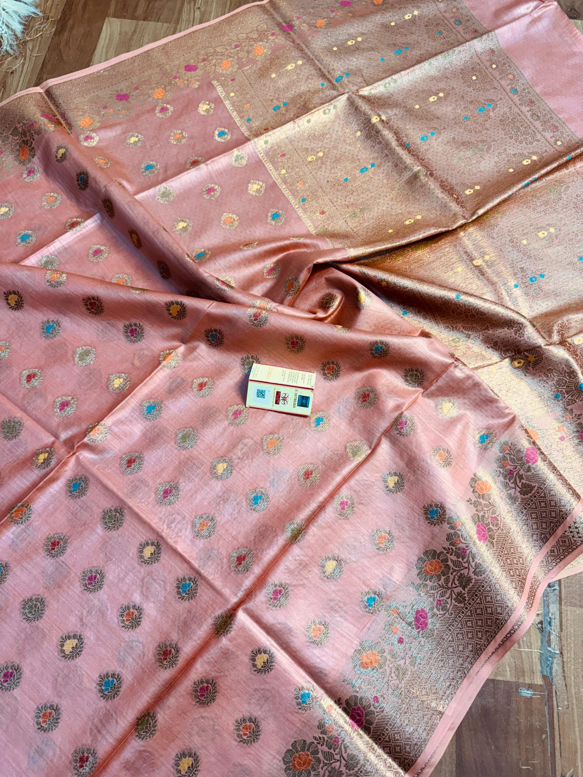 Pastel Peach Pure Bhagalpuri Muga Silk Saree by Bhavya Lakshmi Fabrics Elegant pastel peach pure Bhagalpuri Muga silk saree from Bhavya Lakshmi Fabrics featuring multi-color floral butis and an intricate gold zari border