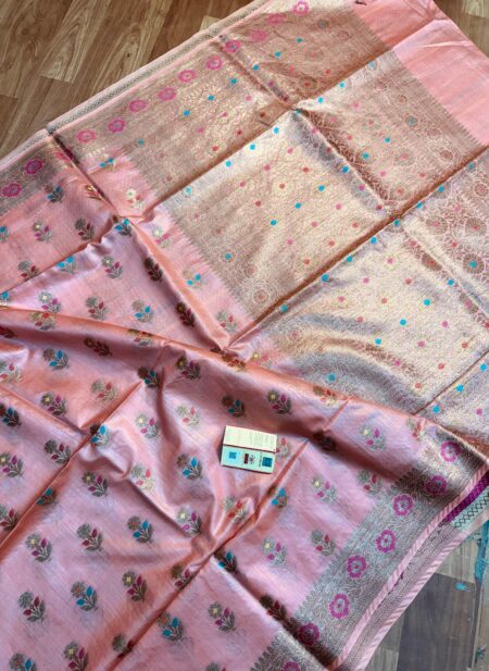 Elegant pastel peach pure Bhagalpuri Munga silk saree from Bhavya Lakshmi Fabrics featuring multi-color floral butis and an intricate gold zari border, spread on a wooden floor.