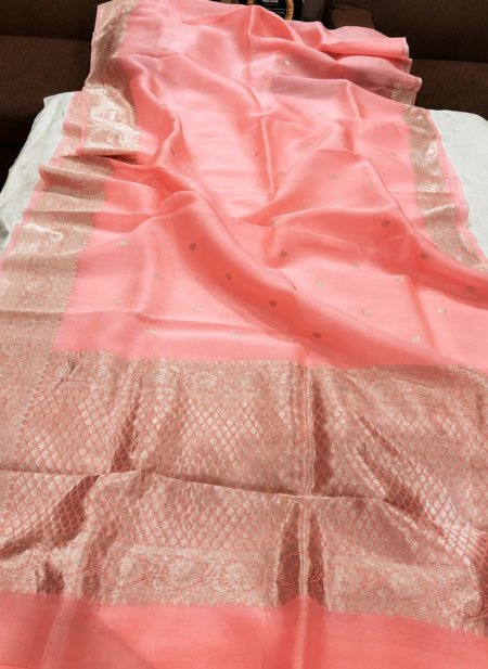 A close-up view of a serene Peach Organza Banarasi Saree from Bhavya Lakshmi Fabrics featuring detailed handwoven metallic zari borders and delicate scattered butis.