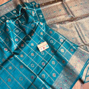 Vibrant peacock blue pure Bhagalpuri Munga silk saree from Bhavya Lakshmi Fabrics featuring gold zari checks with multi-color floral Meenakari butis and an intricate gold zari border, spread on a wooden floor.