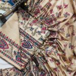 An unstitched cream Katan silk suit material set by Bhavya Lakshmi Fabrics featuring detailed multi-colored Madhubani prints of ceremonial elephants, peacocks, and floral creepers in magenta pink and indigo blue.