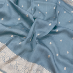A close-up view of a serene Powder Blue Organza Banarasi Saree from Bhavya Lakshmi Fabrics featuring detailed handwoven silver zari floral borders and delicate scattered buti