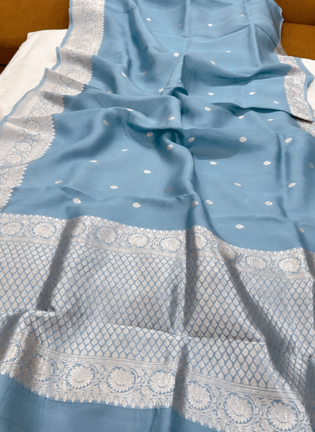A close-up view of a serene Powder Blue Organza Banarasi Saree from Bhavya Lakshmi Fabrics featuring detailed handwoven silver zari floral borders and delicate scattered butis