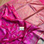 Vibrant Rani pink pure Bhagalpuri Munga silk saree from Bhavya Lakshmi Fabrics featuring multi-color floral butis and an intricate gold zari border, spread on a wooden floor.