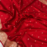 A close-up view of a vibrant Red Organza Banarasi Saree from Bhavya Lakshmi Fabrics featuring detailed handwoven golden zari floral borders and delicate scattered butis
