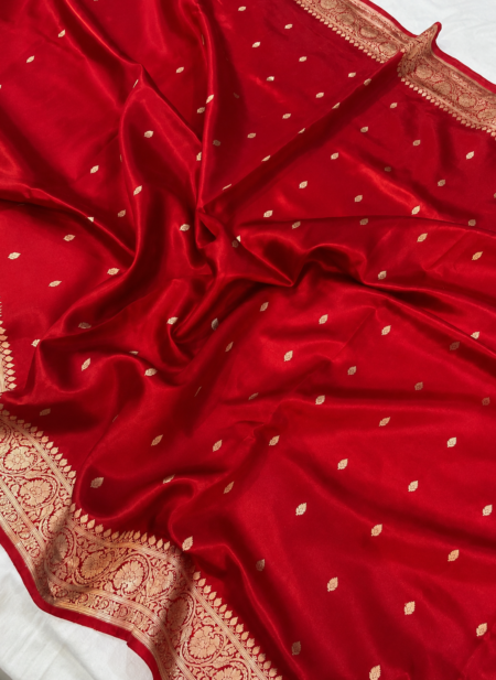 A close-up view of a vibrant Red Organza Banarasi Saree from Bhavya Lakshmi Fabrics featuring detailed handwoven golden zari floral borders and delicate scattered butis
