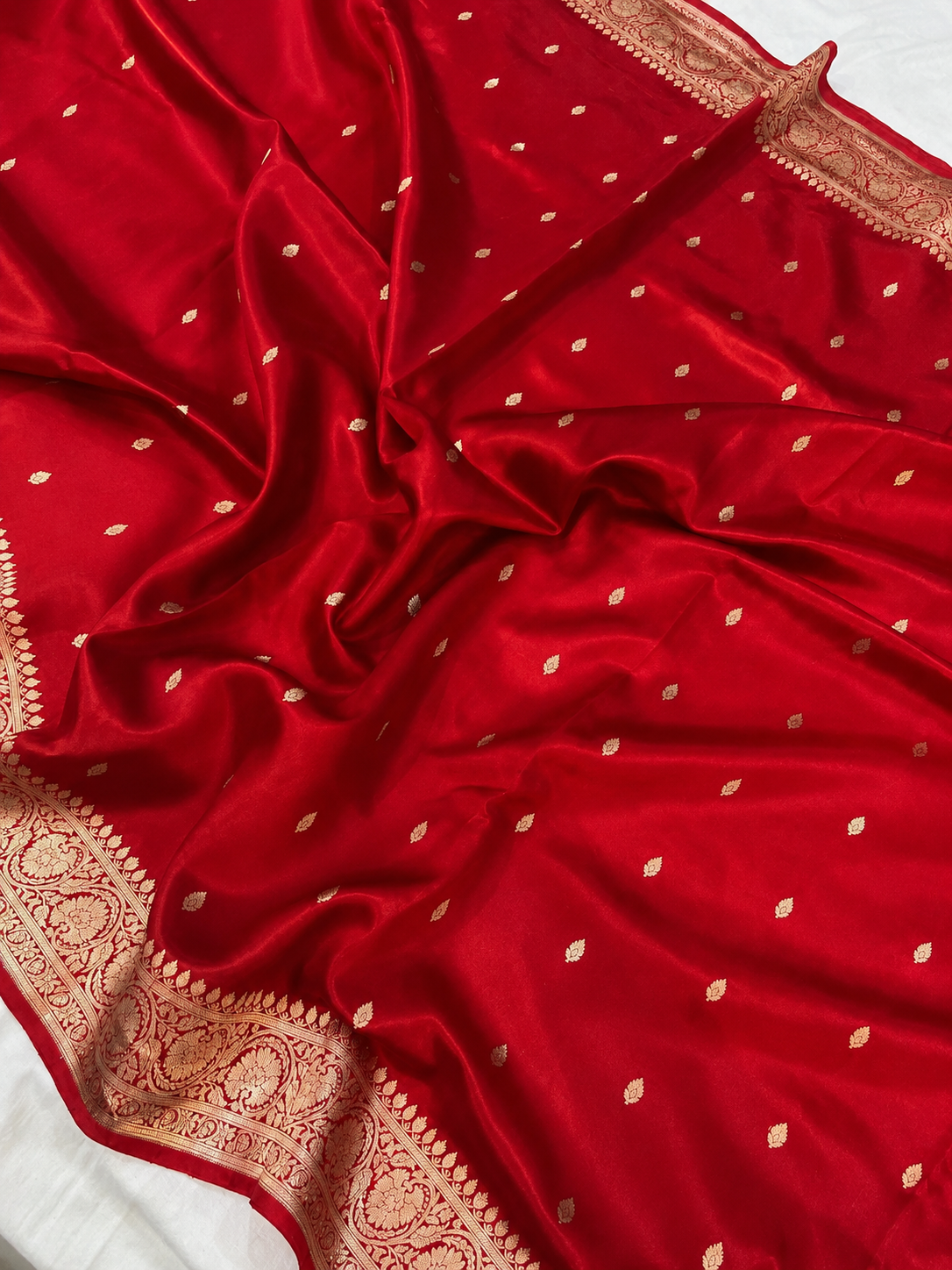 Red Organza Banarasi Saree by Bhavya Lakshmi Fabrics A close-up view of a vibrant Red Organza Banarasi Saree from Bhavya Lakshmi Fabrics featuring detailed handwoven golden zari floral borders and delicate scattered butis