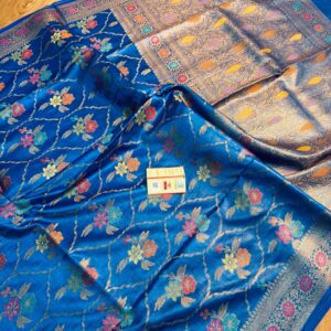 Vibrant royal blue pure Bhagalpuri Munga silk saree from Bhavya Lakshmi Fabrics featuring a multi-color floral Meenakari jaal and an intricate gold zari border, spread on a wooden floor