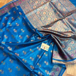Vibrant royal blue pure Bhagalpuri Munga silk saree from Bhavya Lakshmi Fabrics featuring multi-color floral butis and an intricate gold zari border, spread on a wooden floor.