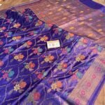 Vibrant royal purple pure Bhagalpuri Munga silk saree from Bhavya Lakshmi Fabrics featuring a multi-color floral Meenakari jaal and an intricate gold zari border, spread on a wooden floor.