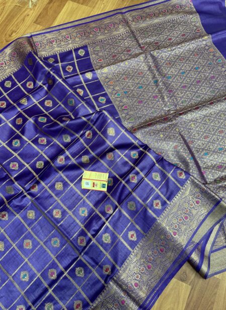 Vibrant royal purple pure Bhagalpuri Munga silk saree from Bhavya Lakshmi Fabrics featuring gold zari checks with multi-color floral Meenakari butis and an intricate gold zari border, spread on a wooden floor.