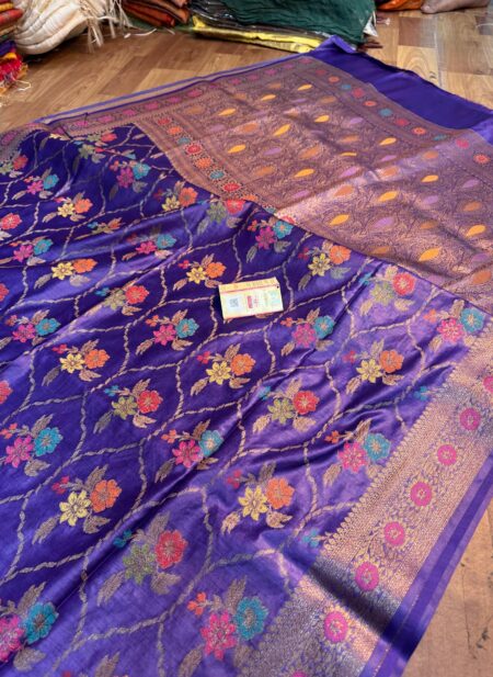 Vibrant royal purple pure Bhagalpuri Munga silk saree from Bhavya Lakshmi Fabrics featuring a multi-color floral Meenakari jaal and an intricate gold zari border, spread on a wooden floor.