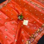 A vibrant rust orange pure Bhagalpuri Munga silk handloom saree from Bhavya Lakshmi Fabrics featuring detailed multicolored floral embroidery scattered butis and an ornate floral border.