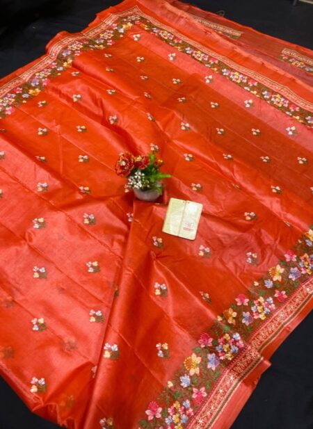 A vibrant rust orange pure Bhagalpuri Munga silk handloom saree from Bhavya Lakshmi Fabrics featuring detailed multicolored floral embroidery scattered butis and an ornate floral border.